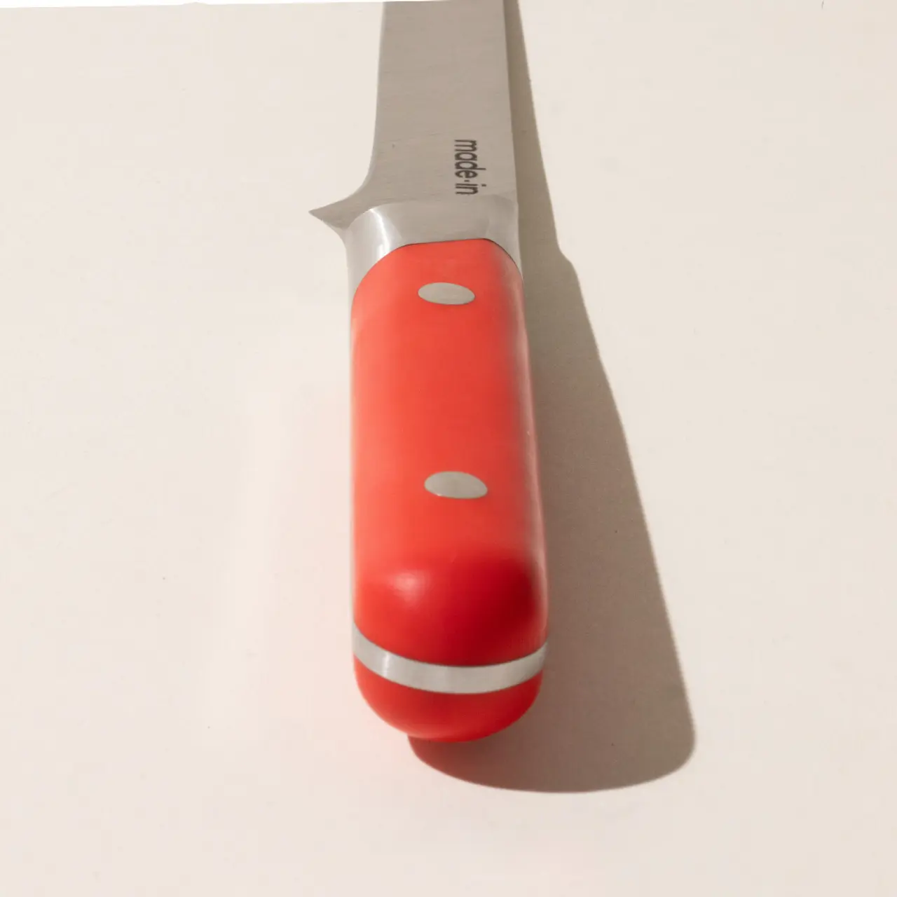 A knife with a red handle lies on a plain surface, casting a slight shadow.