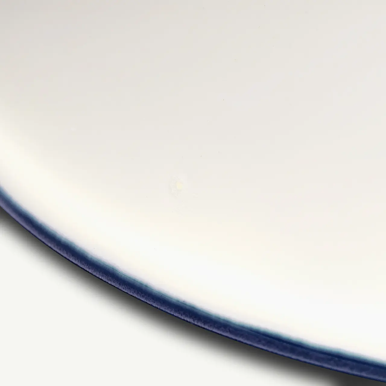 A close-up of a white ceramic plate with a smooth surface and a blue rim.