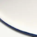 A close-up of a white ceramic plate with a smooth surface and a blue rim.
