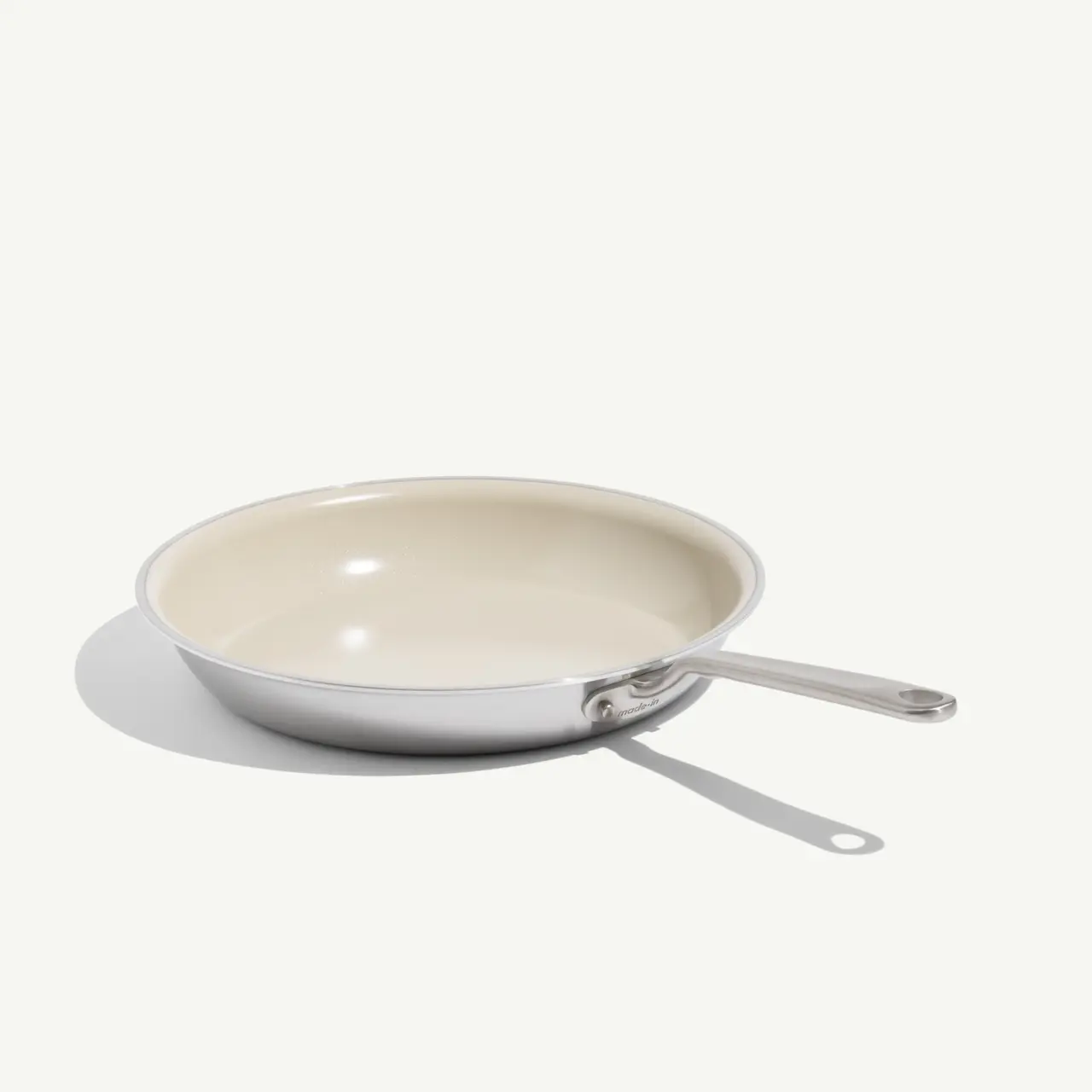 A stainless steel frying pan with a cream-colored interior and a sleek handle.