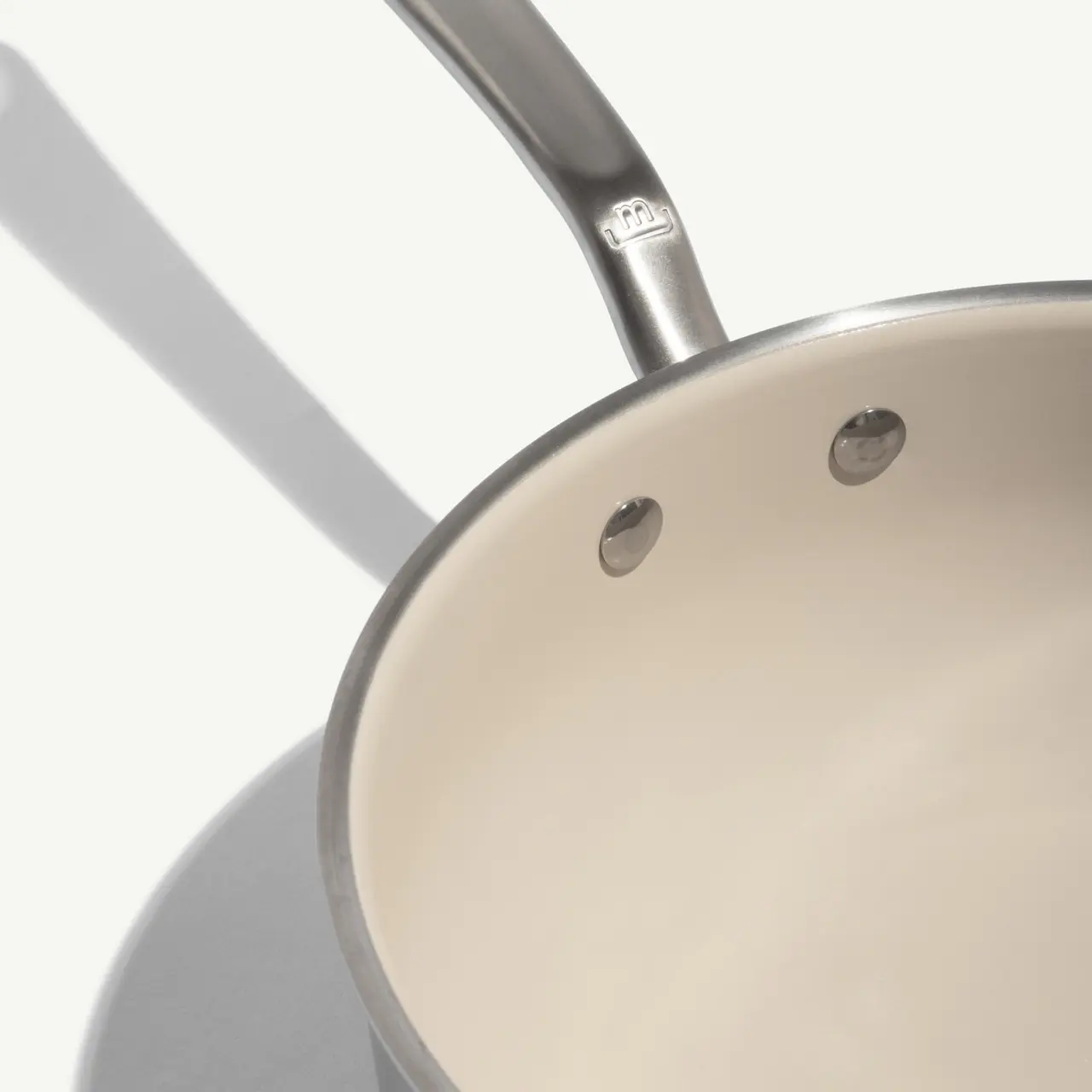 A stainless steel saucepan with a curved handle and two rivets on the side.