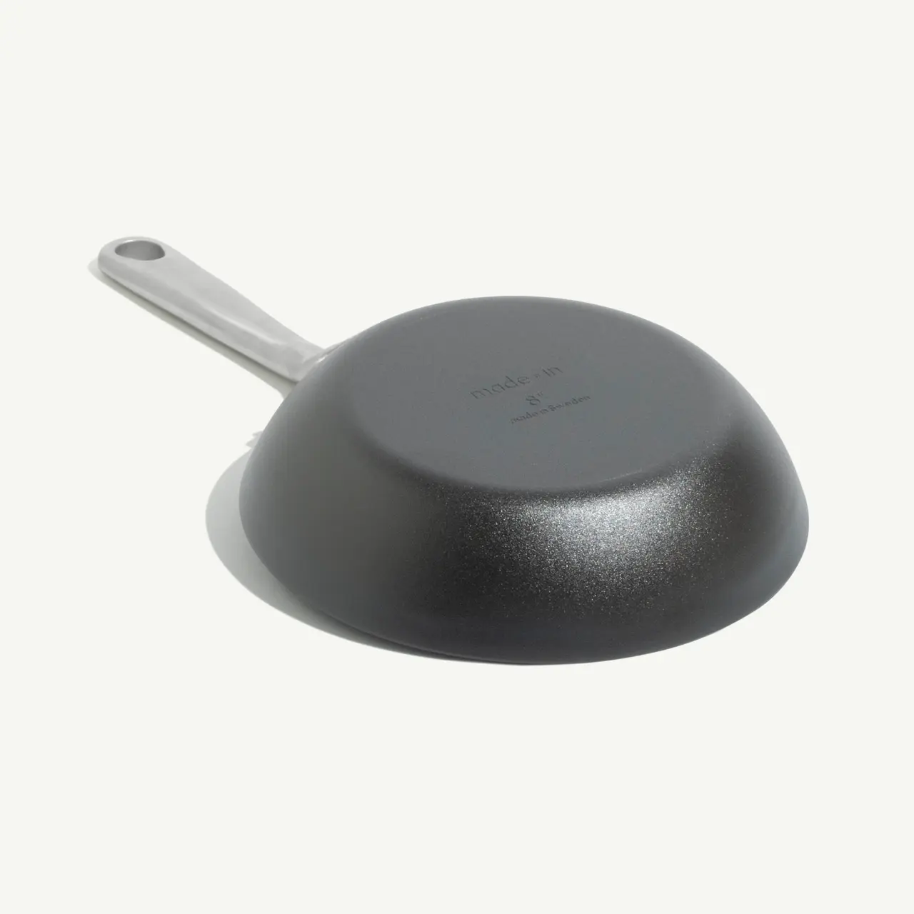A black, round frying pan with a stainless steel handle sits on a neutral background.