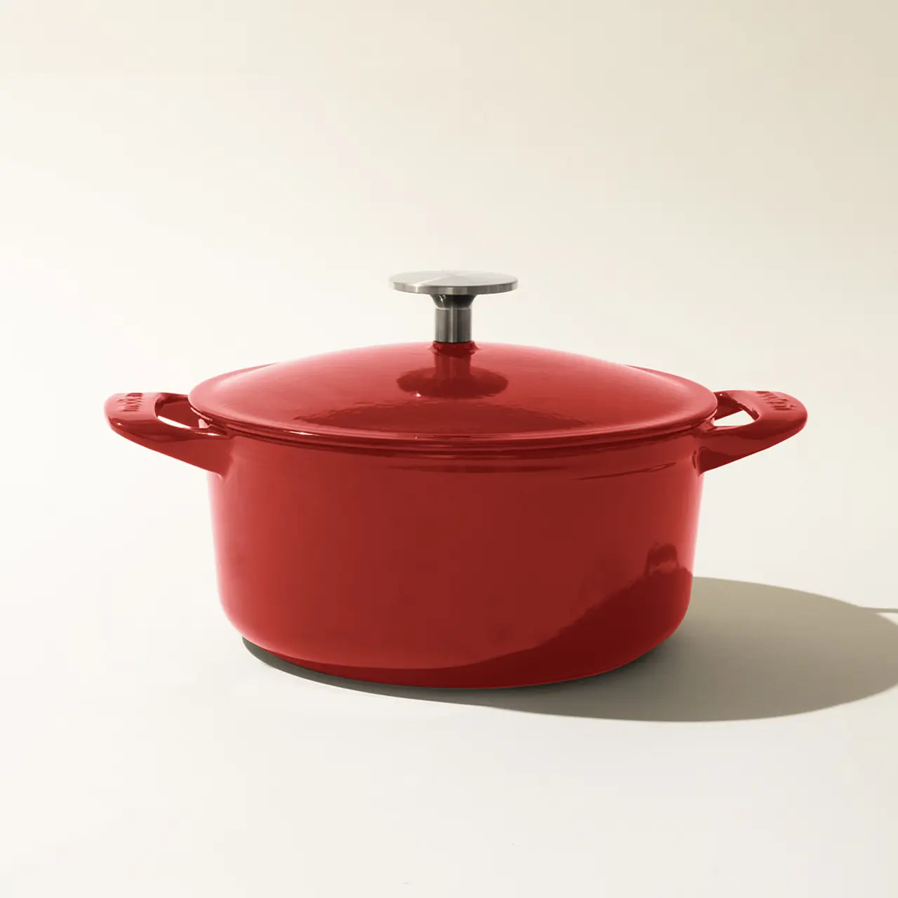 A red enameled cast iron Dutch oven with a lid, placed on a light background.