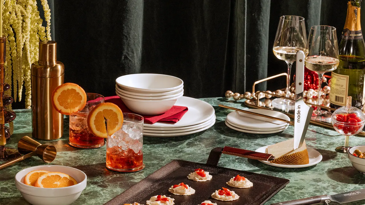 A luxurious dining setup with cocktails, appetizers on a slate serving board, and elegant tableware on a dark velvet cloth.