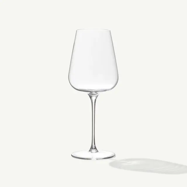 A clear, empty wine glass stands upright with its shadow cast to the right.
