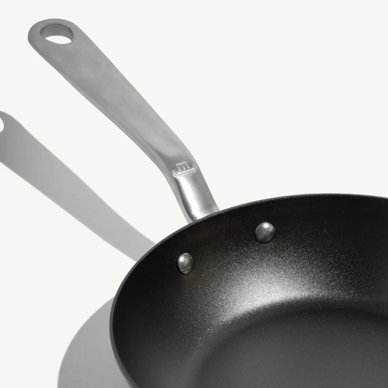 A stainless steel frying pan with a non-stick surface and a long handle is displayed against a plain background.