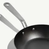 A stainless steel frying pan with a non-stick surface and a long handle is displayed against a plain background.