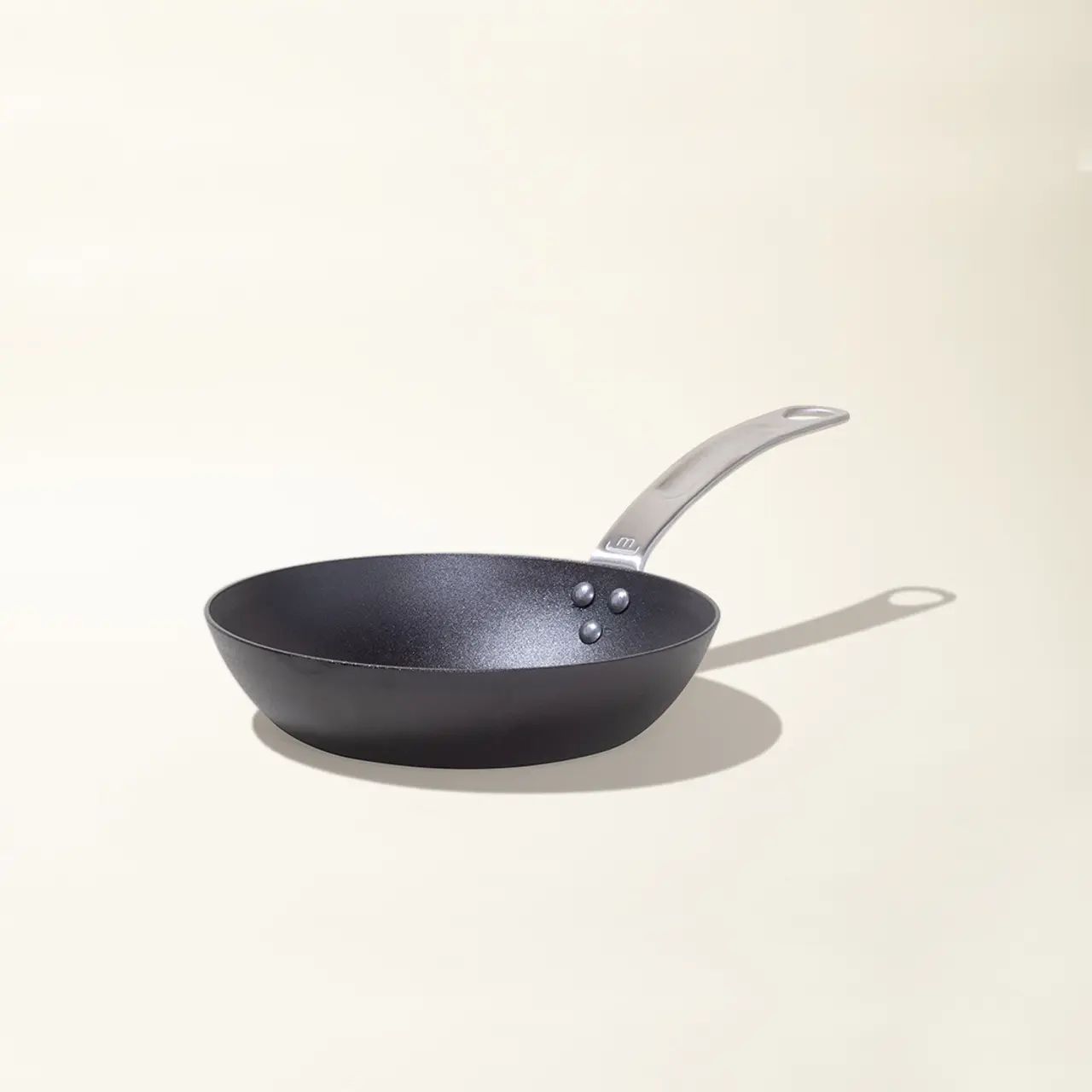 A black frying pan with a silver handle is centered against a light background.
