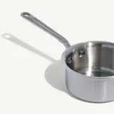 A stainless steel saucepan with a long handle is placed against a plain background.