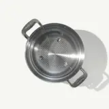 A stainless steel colander with handles is shown from a top view, casting a shadow to the right.