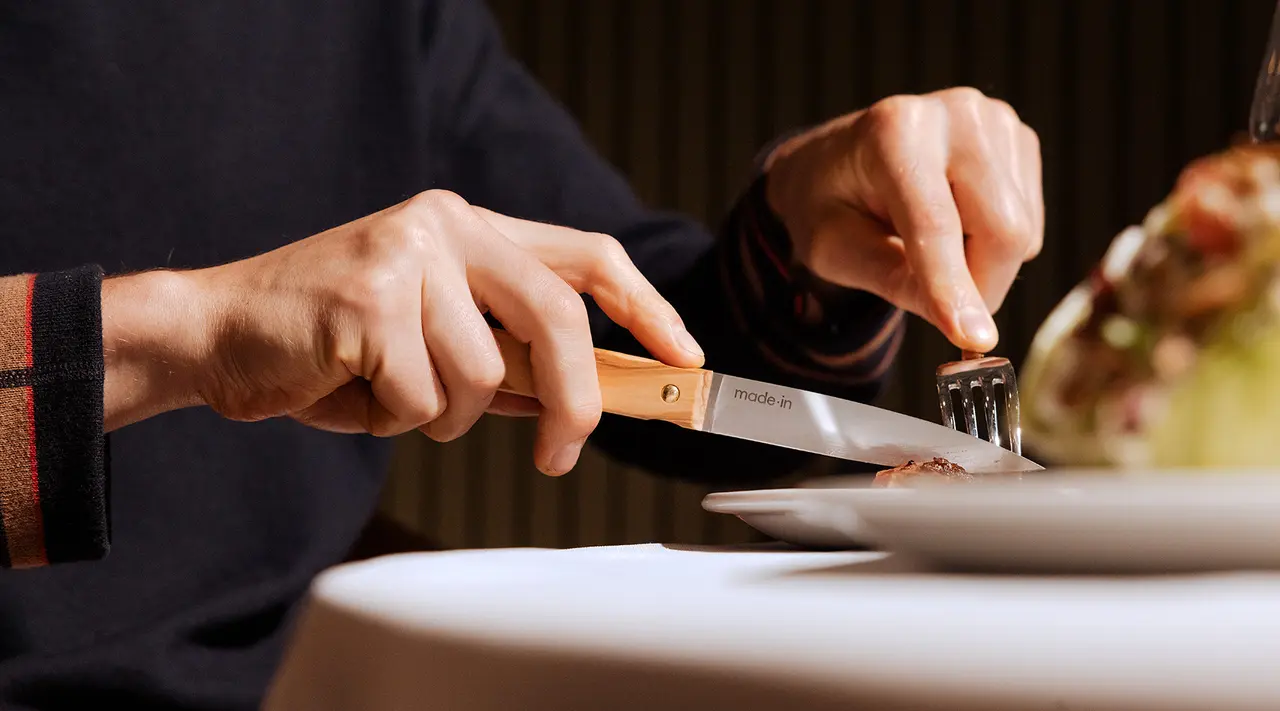 A person is cutting food on a white plate with a knife and fork in a fine dining setting.