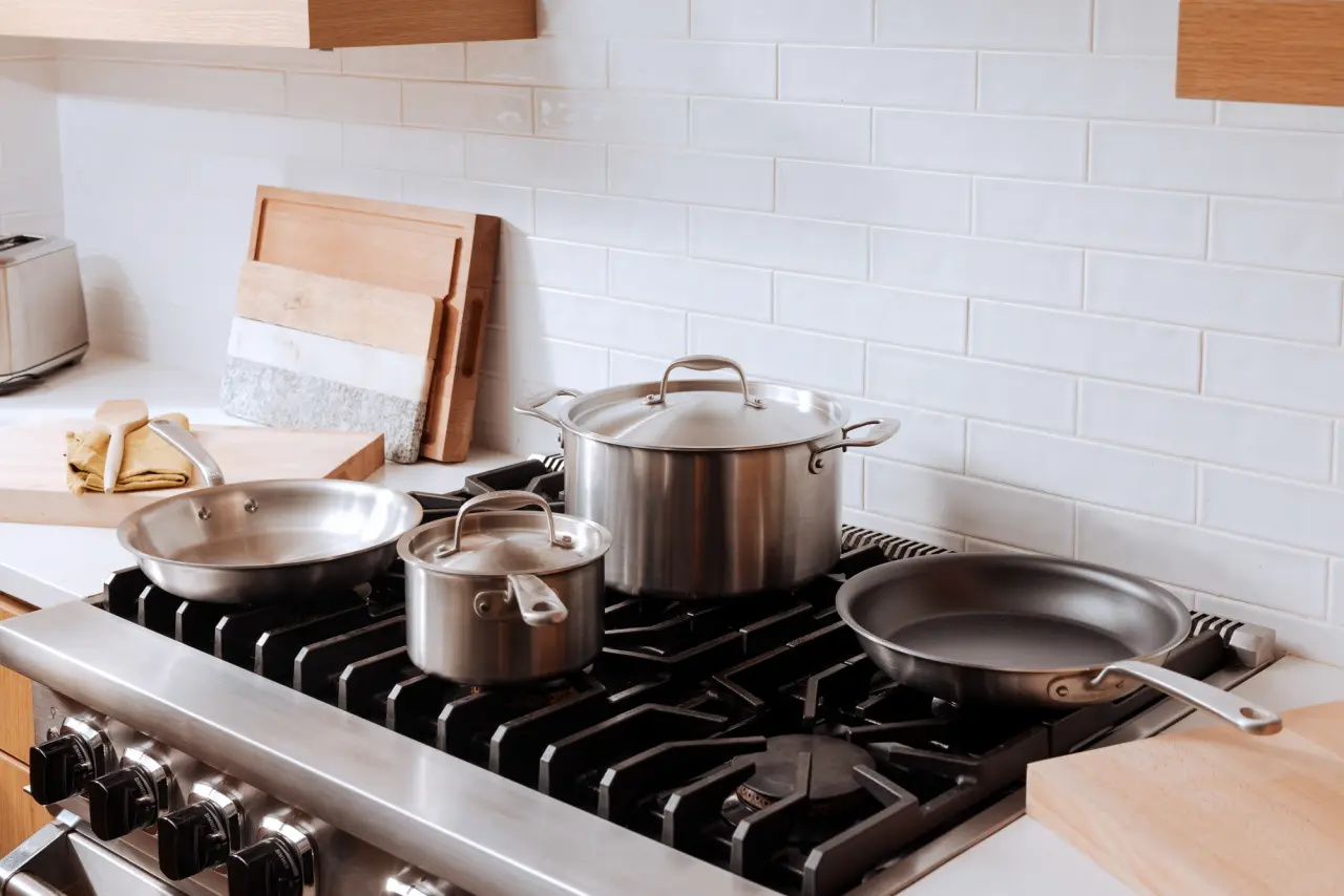 A variety of stainless steel cookware, including pots and pans, is arranged on a gas stove in a modern kitchen setting.