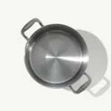A stainless steel saucepan with two handles is pictured from above, casting a shadow on a light background.