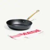 A black frying pan with a golden handle is placed beside a red and white kitchen towel that says "MADE."