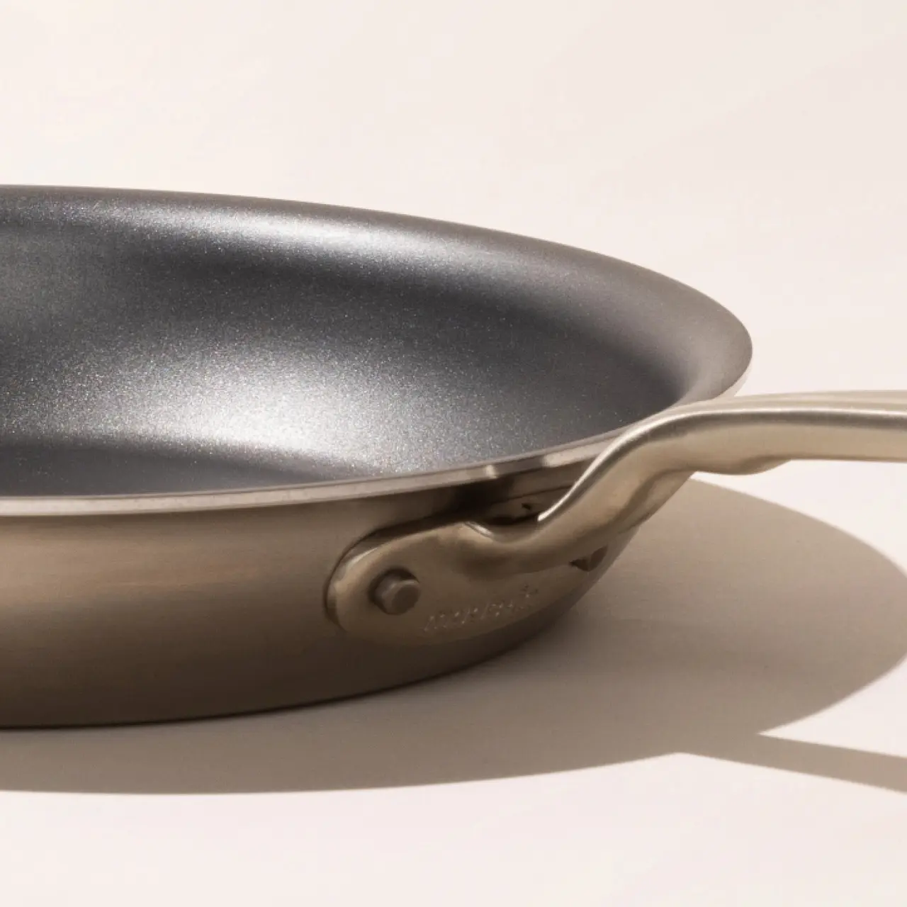 A close-up of a silver frying pan with a stainless steel handle, against a neutral background.
