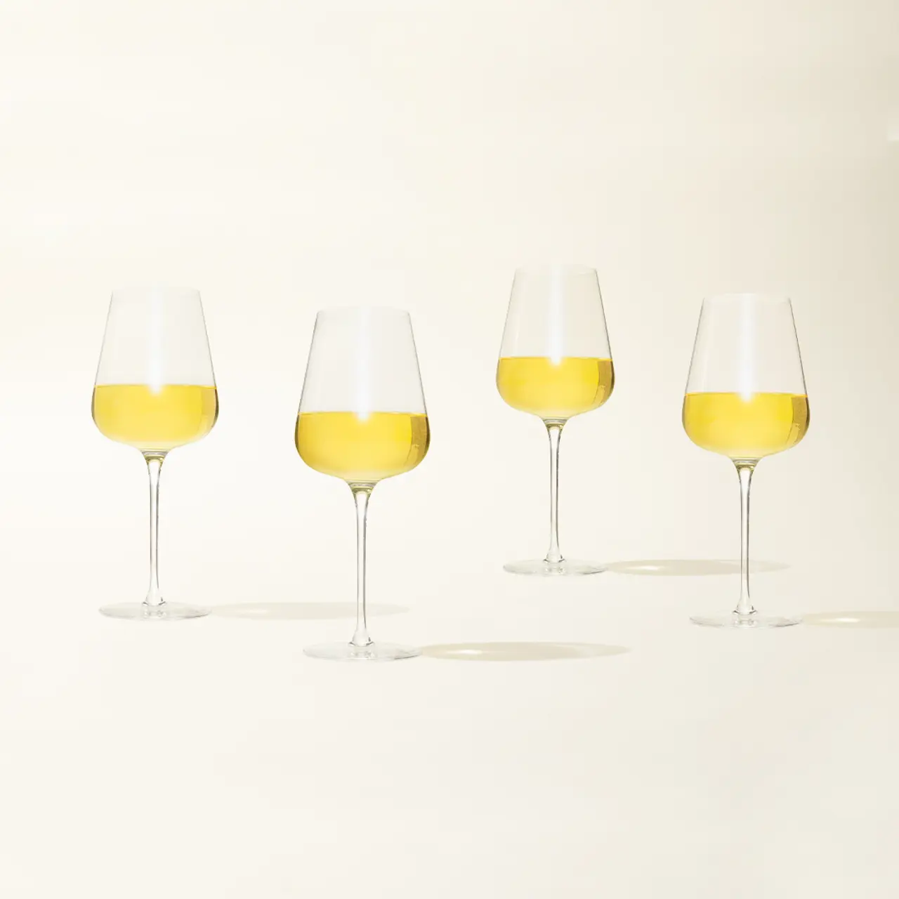 Four wine glasses filled with white wine are lined up against a light background.