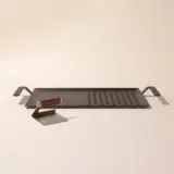 A minimalist designed cheese grater with a sleek metal body and a piece of cheese placed on the side on a light background.