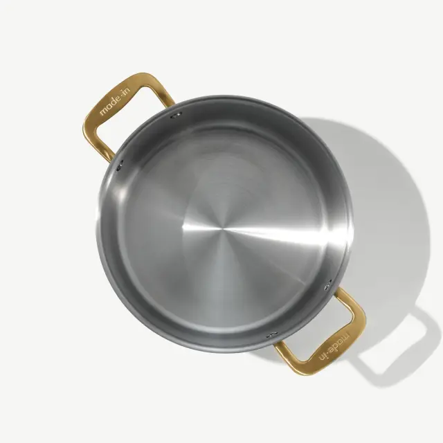 A stainless steel pan with two gold handles, viewed from above on a light background.