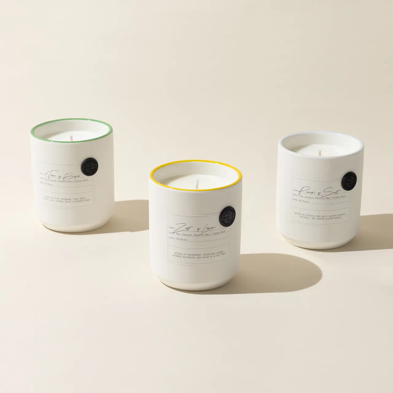 Three scented candles with labels are neatly positioned side by side on a light background, one of which has a distinct yellow rim.