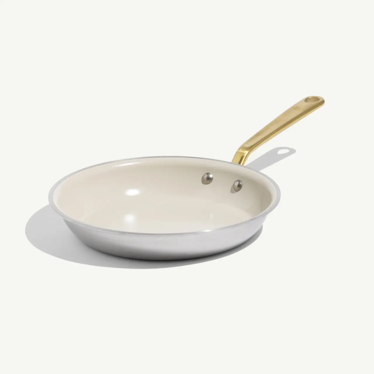 A frying pan with a sleek white nonstick interior and a gold-tone handle sits on a light background.