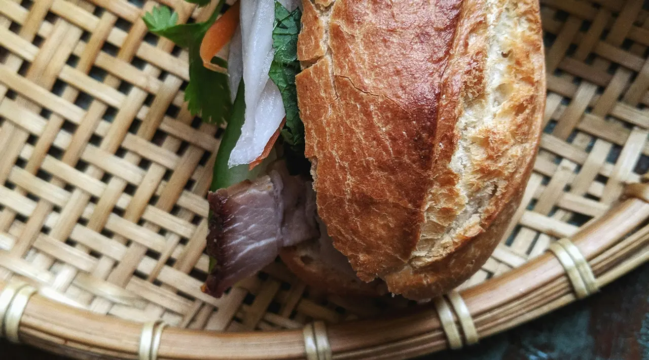 A freshly made sandwich filled with meat and vegetables is placed on a woven basket.