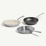 Three frying pans in different materials and colors are arranged on a light background.