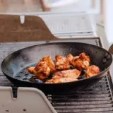 A frying pan with seasoned chicken wings sits on a grill pan.