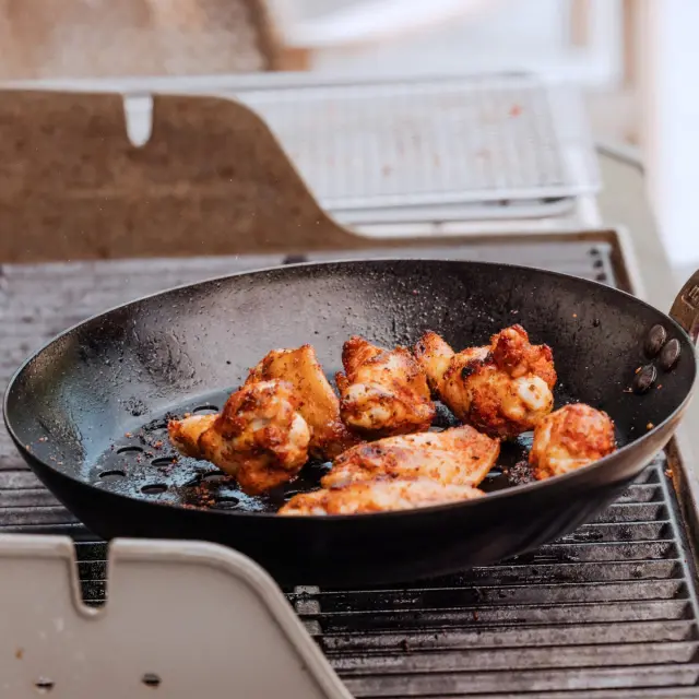 A frying pan with seasoned chicken wings sits on a grill pan.