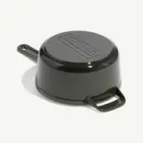 A dark green cast iron pan is shown upside down with a textured base and a handle.