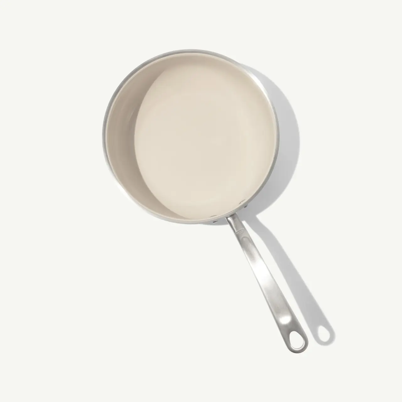 A stainless steel saucepan with a long handle sits on a light background.