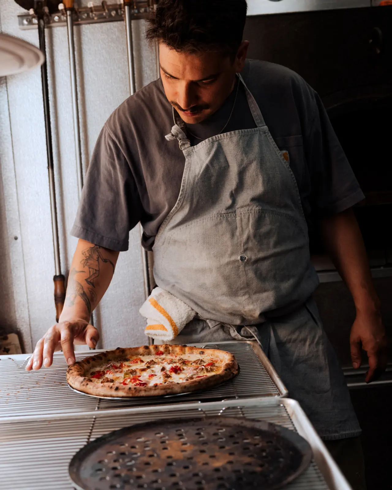 A focused chef is carefully inspecting a freshly baked pizza in a kitchen setting.