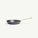 A sleek black frying pan with a gold handle is positioned against a light background.