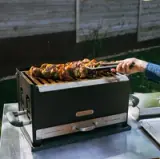 A person is using tongs to turn skewers of colorful grilled vegetables and meat on a BBQ grill outdoors.