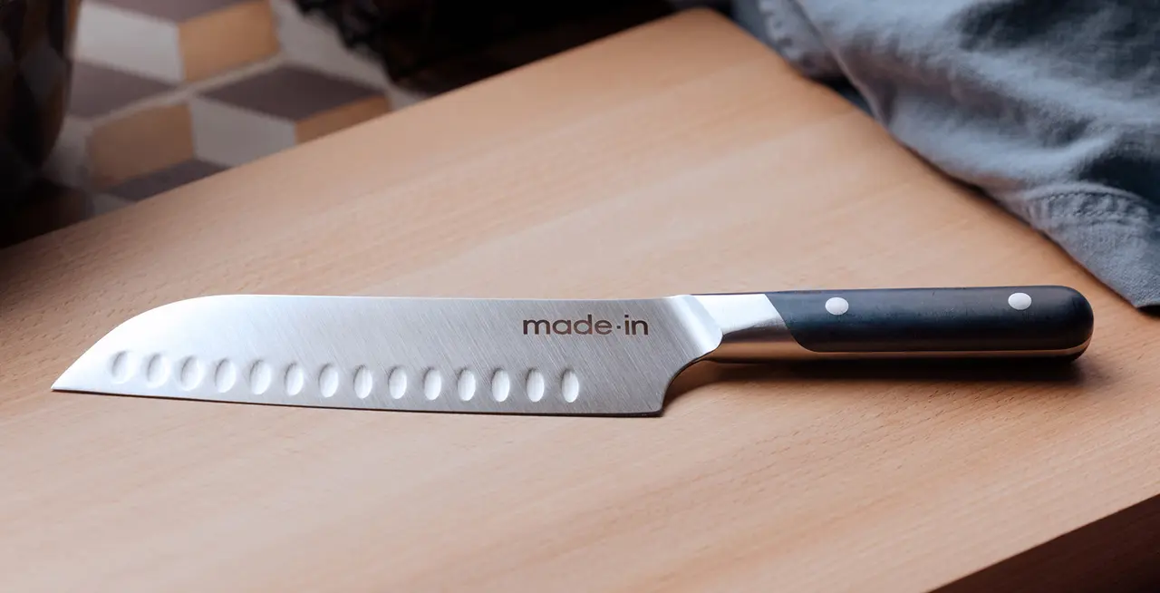 A chef's knife with a black handle and "made.in" branding lies on a wooden surface.
