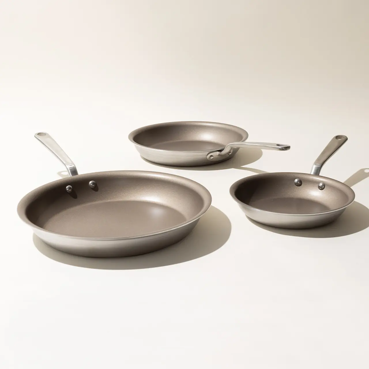 Three different-sized, non-stick frying pans with metallic handles are arranged on a light background.