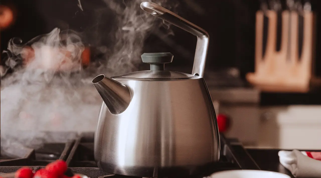 A stainless steel kettle emits steam while sitting on a stovetop, surrounded by a cozy kitchen setting.