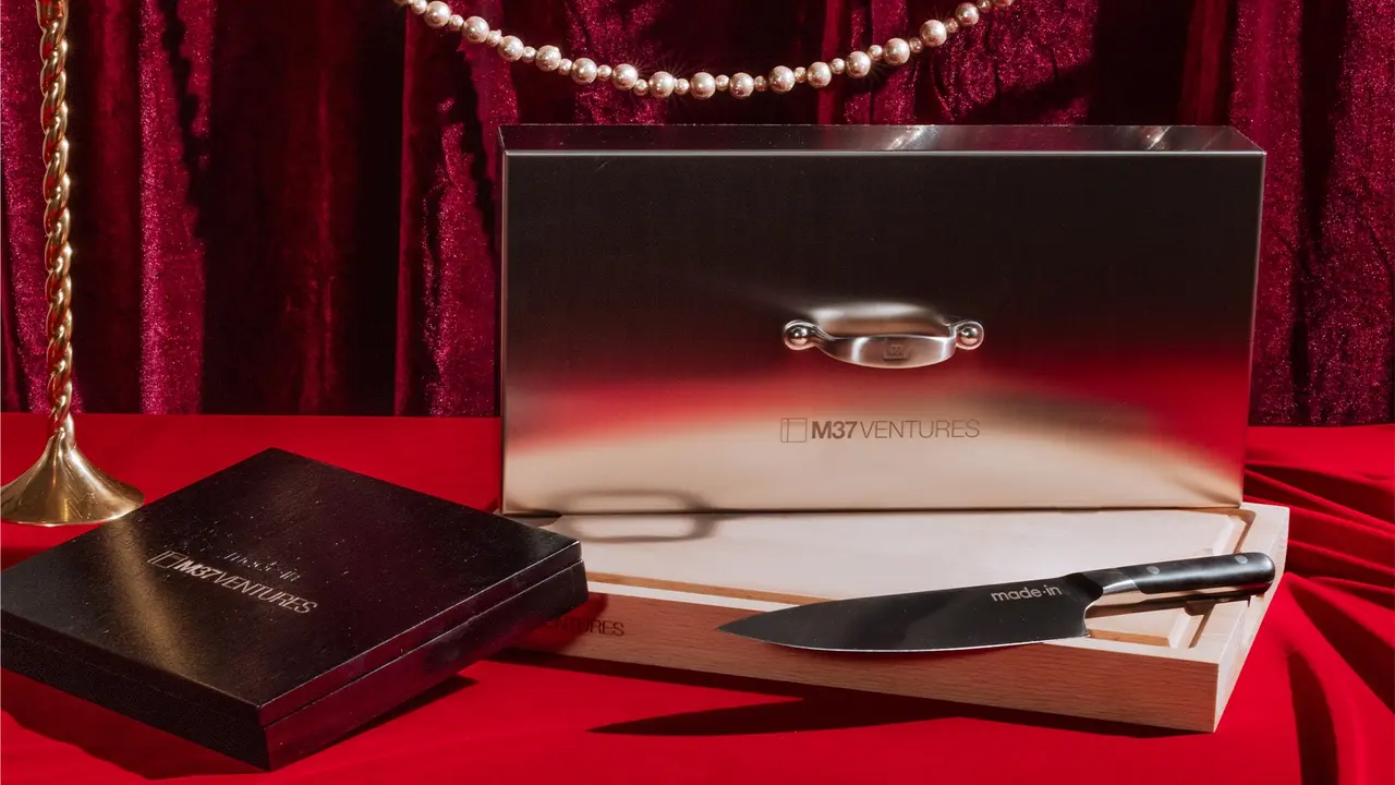 A luxury pen set is presented on a red surface with velvet curtains in the background, accompanied by a string of pearls and an embossed box.