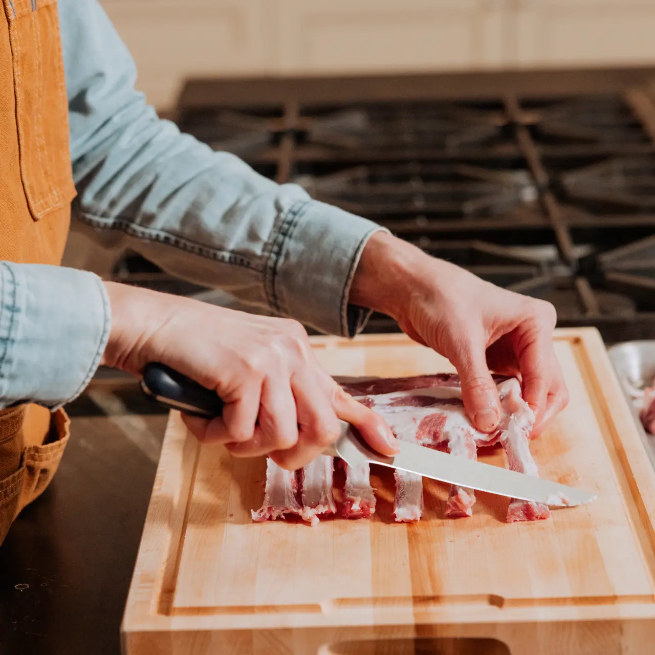 A person wearing an apron is cutting raw meat on a wooden chopping board.