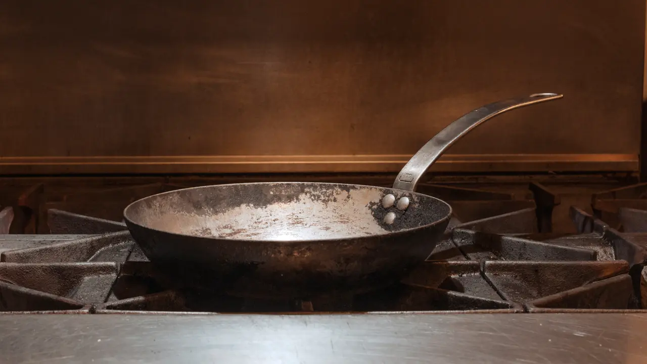 A well-used frying pan sits atop a gas stove burner.