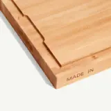 A wooden cutting board with the words "MADE IN" engraved on the side edge.