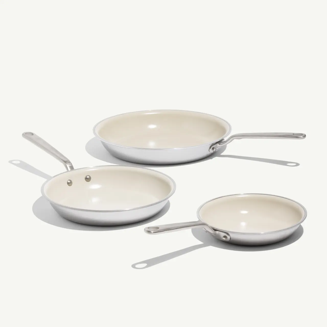 Three non-stick frying pans of varying sizes are arranged in a staggered formation against a light background.