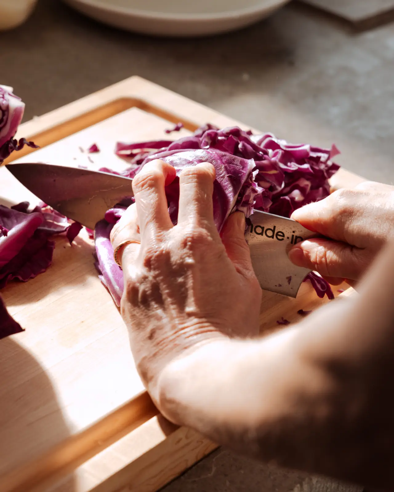 Hands are chopping red cabbage on a wooden cutting board.