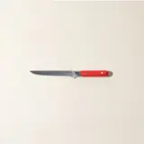 A single kitchen knife with a red handle lies centered on a plain beige background.