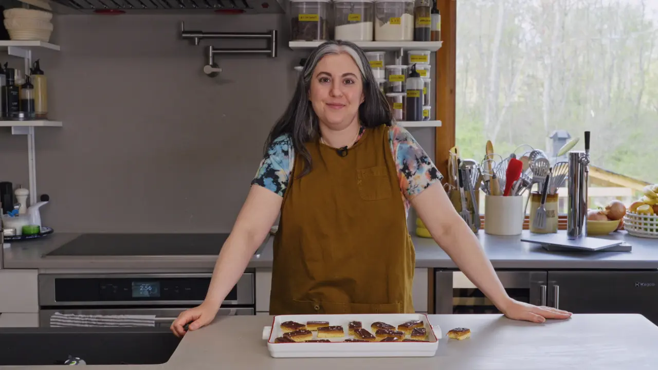 A person is standing in a kitchen with a tray of pastries placed on a countertop, smiling at the camera.