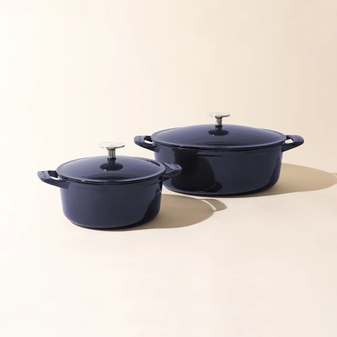 Two blue enameled cast iron pots with lids on a beige background.