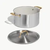 A stainless steel pot with a white interior and golden handles, accompanied by a matching lid.