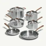A collection of six stainless steel cookware pieces with copper handles, including various pots and frying pans.