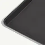 A non-stick baking sheet is shown from a corner perspective against a plain background.