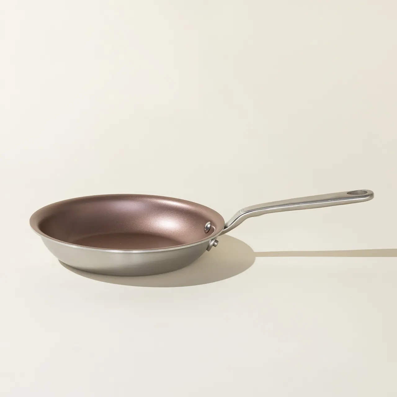 A solitary non-stick frying pan with a stainless steel handle is positioned on a neutral background, casting a soft shadow.
