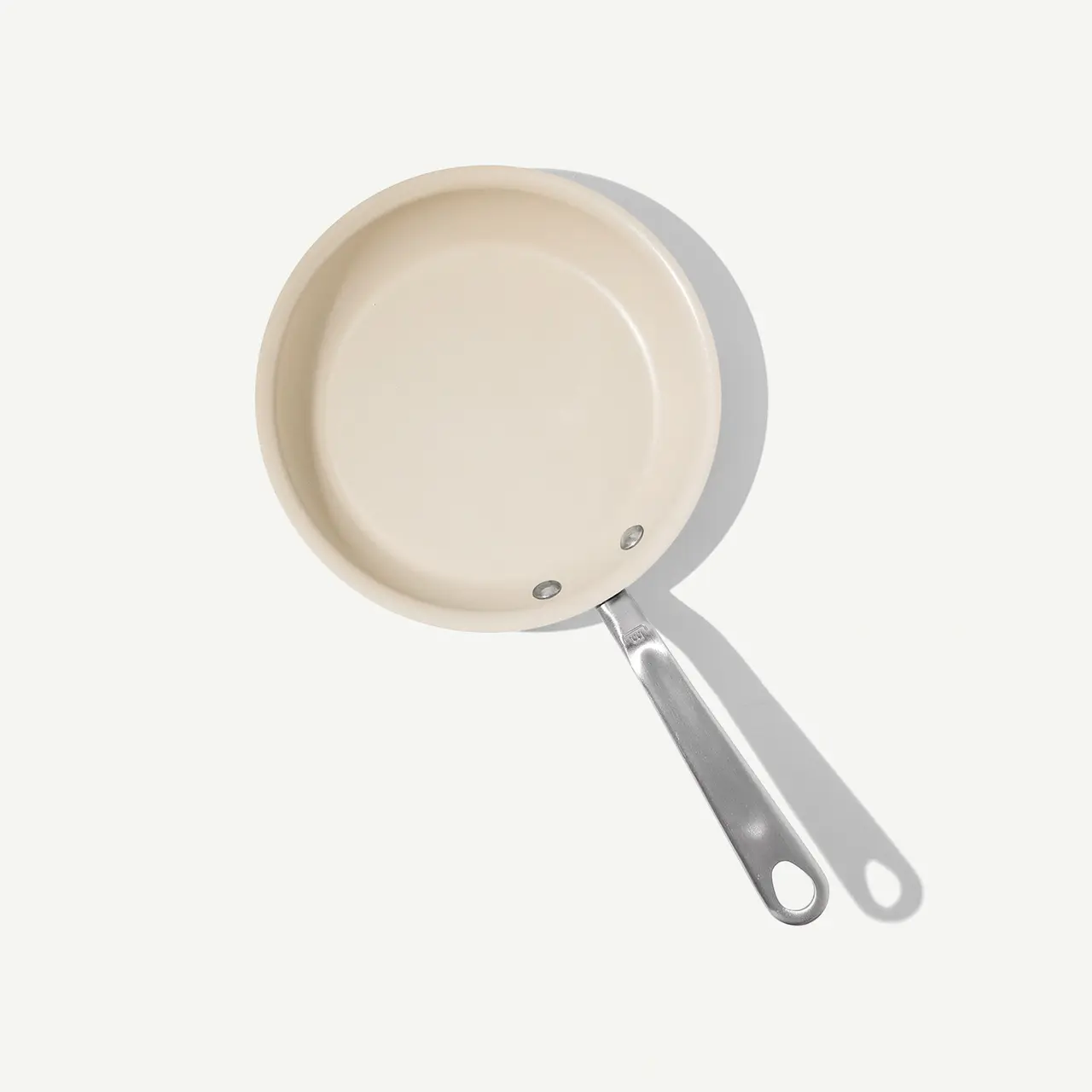 A beige frying pan with a silver handle on a light background, viewed from above.